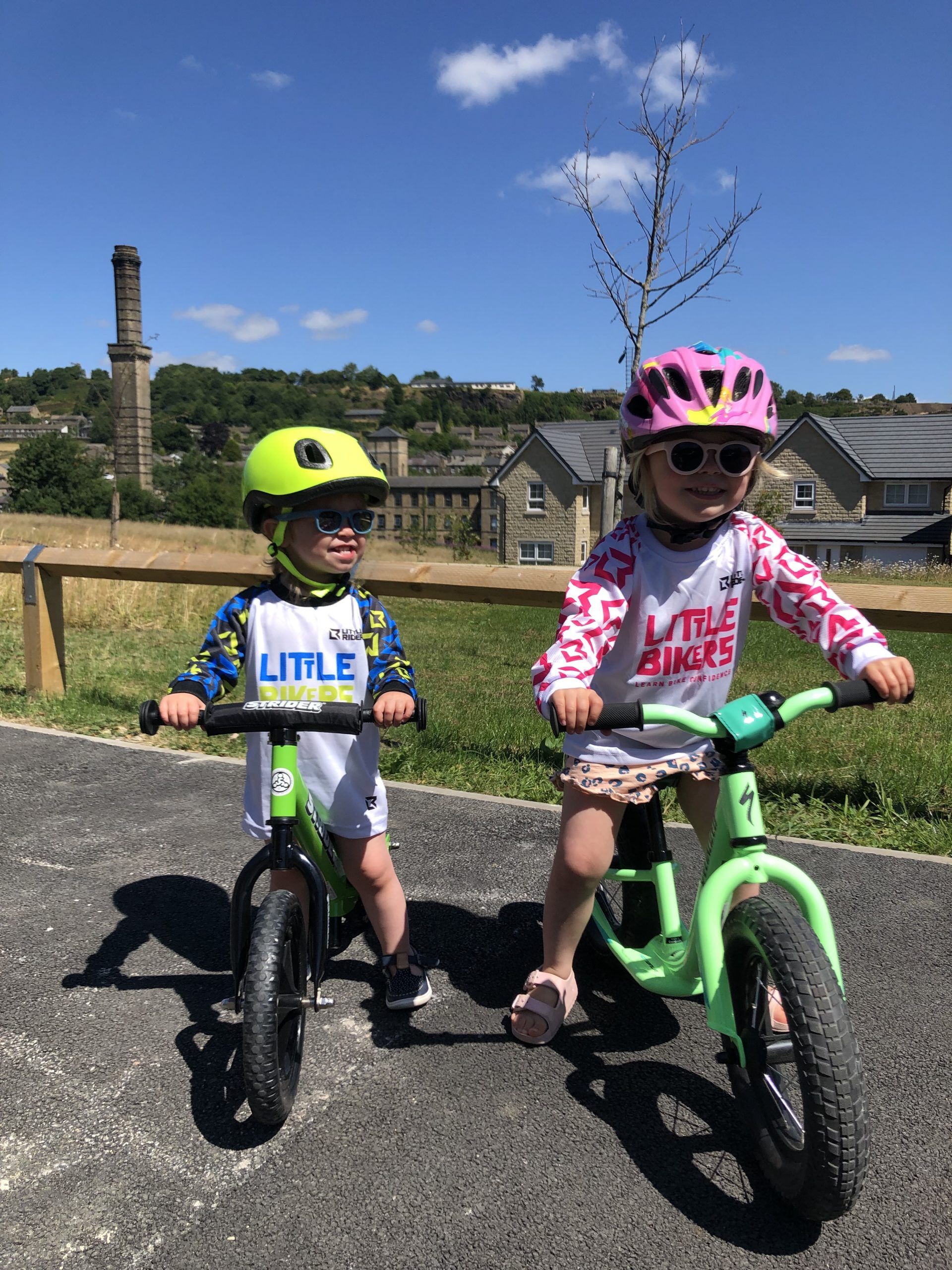 A boy and a girl, smiling on their balance bikes.